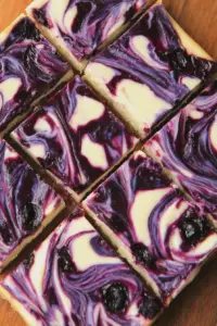 Delicious blueberry swirl cheesecake bars garnished with fresh blueberries and mint on a white plate.