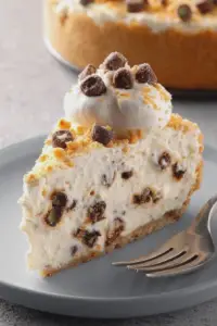 Delicious cannoli cheesecake slice with chocolate chips and pistachios on a plate.