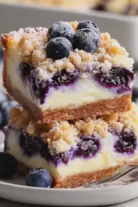 Creamy blueberry cheesecake bars with fresh blueberries and powdered sugar on a rustic wooden table.
