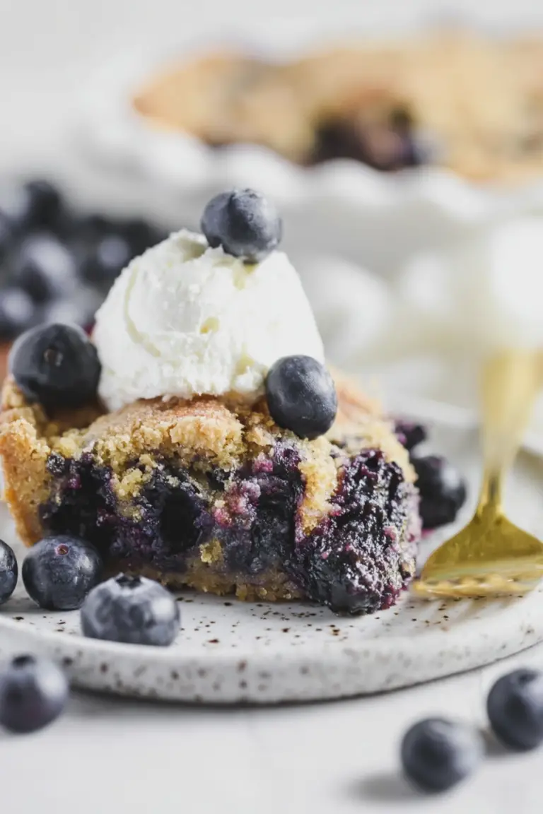 A delicious slice of crustless blueberry pie topped with whipped cream and fresh blueberries on a wooden table.