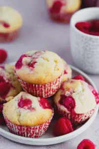 Freshly baked raspberry muffins cooling on a rack with raspberries scattered around.