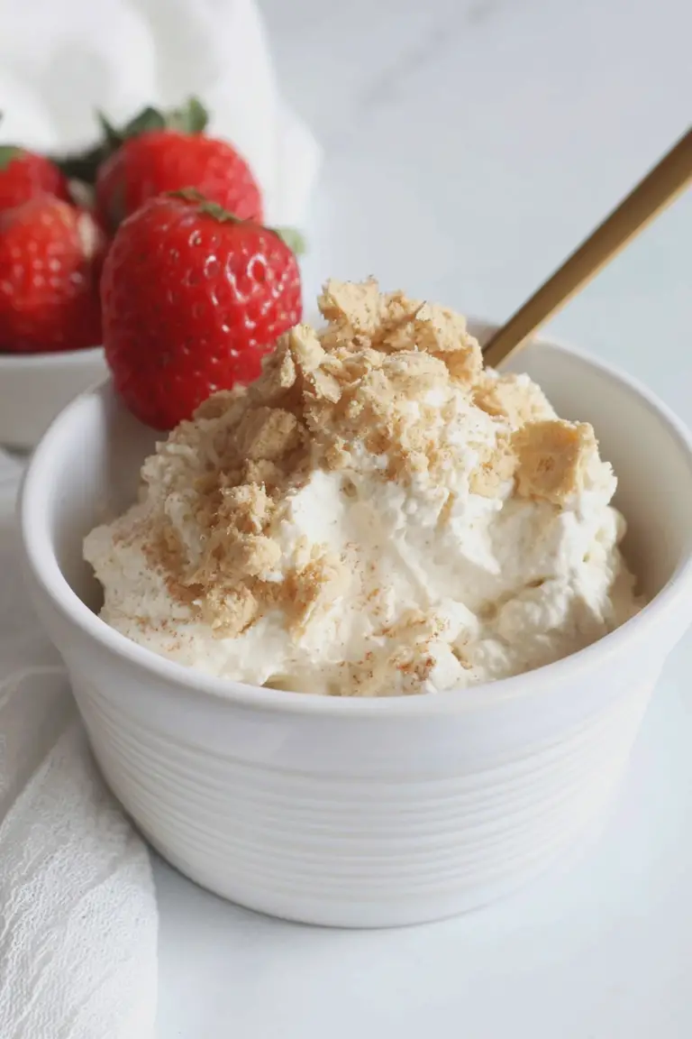 High protein cheesecake fluff topped with fresh strawberries and graham cracker crumbs in a decorative bowl.