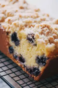 Sliced lemon blueberry loaf with blueberries and lemon slices on a cutting board, drizzled with lemon icing.