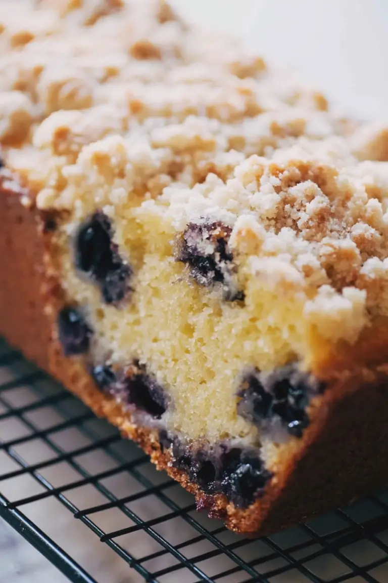 Sliced lemon blueberry loaf with blueberries and lemon slices on a cutting board, drizzled with lemon icing.
