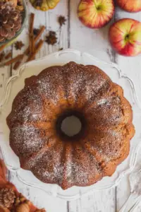 Moist apple spice bundt cake drizzled with bourbon glaze, displayed with fresh apples and spices.