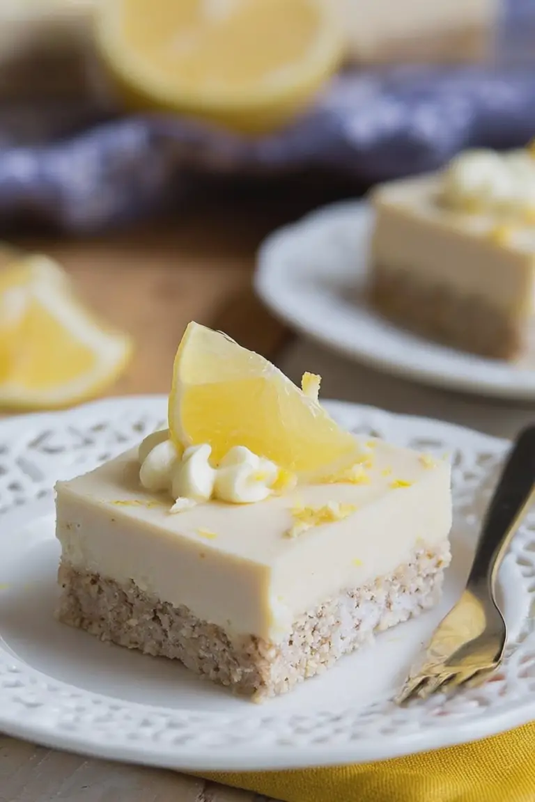 Close-up of a creamy no-bake paleo lemon bar slice on a plate, garnished with lemon zest and mint leaves.