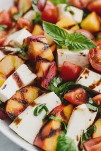 Vibrant Peach Caprese salad with peaches, tomatoes, and mozzarella on a rustic wooden table.
