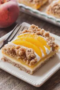 Delicious peach pie crumble bar slice served with fresh peaches and vanilla ice cream on a wooden table.