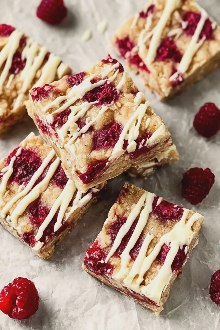Close-up of raspberry and white chocolate squares on a wooden board with fresh raspberries and white chocolate curls.