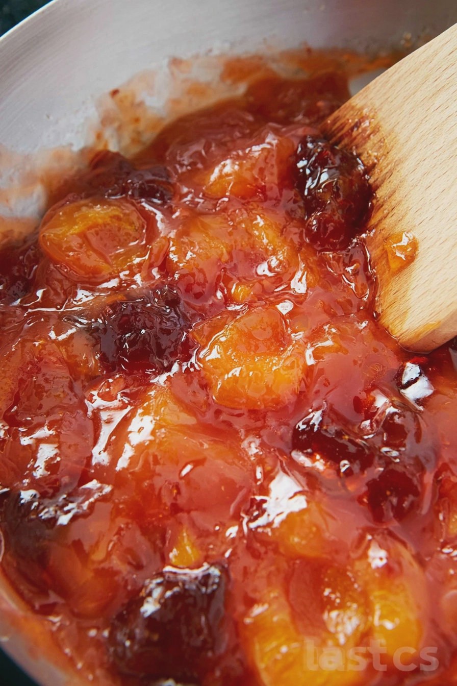 A pot of old-fashioned apricot jam simmering on the stove with fresh apricots and ingredients in a rustic kitchen.