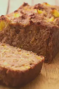 Sliced peach bread loaf on a wooden cutting board, highlighting fresh peach chunks and a moist texture, perfect for breakfast or snacks.