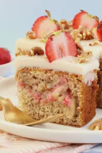 Delicious strawberry banana cake with cream cheese frosting decorated with fresh strawberries and chopped walnuts.