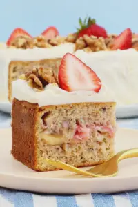 Delicious slice of strawberry banana cake with fresh strawberries and nuts on a rustic wooden table.