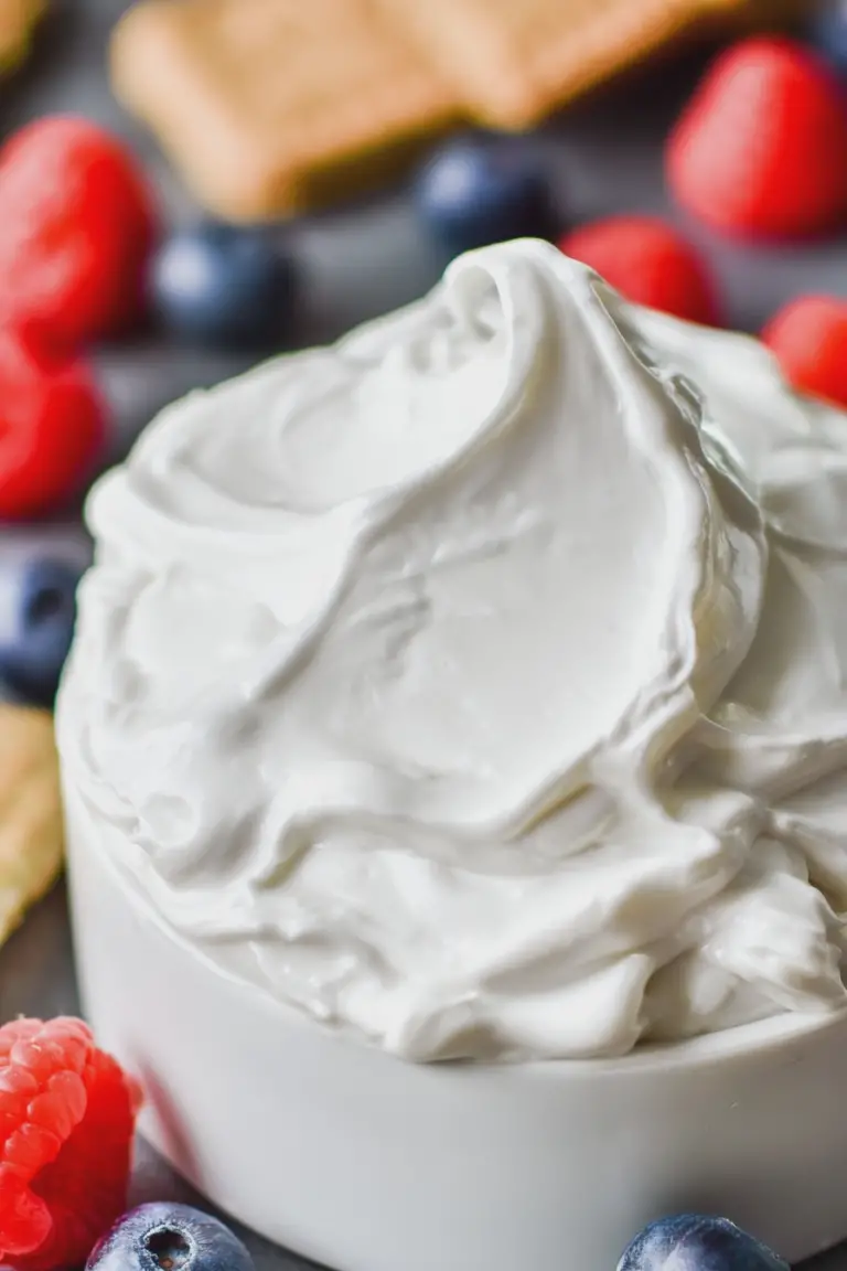 A bowl of creamy whipped Greek yogurt topped with fresh strawberries and blueberries, drizzled with maple syrup.